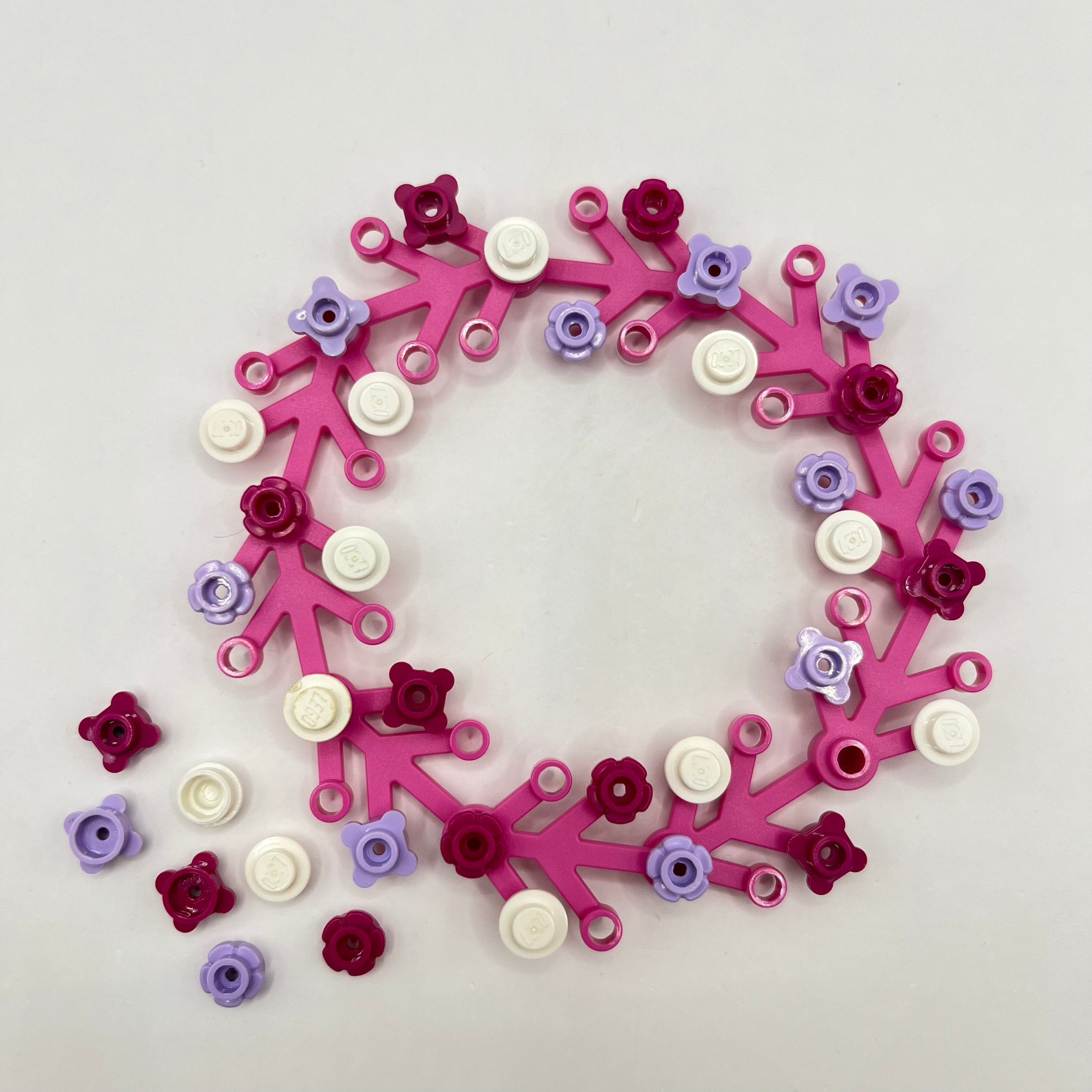 Decorative LEGO Christmas wreath made of interlocking pink, purple, and white pieces on a light grey background